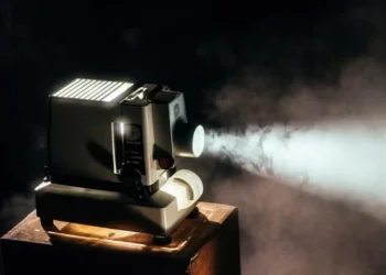 Proiettore cinematografico d'epoca acceso che proietta un fascio di luce in una stanza buia, con il fumo che rende visibile il raggio luminoso