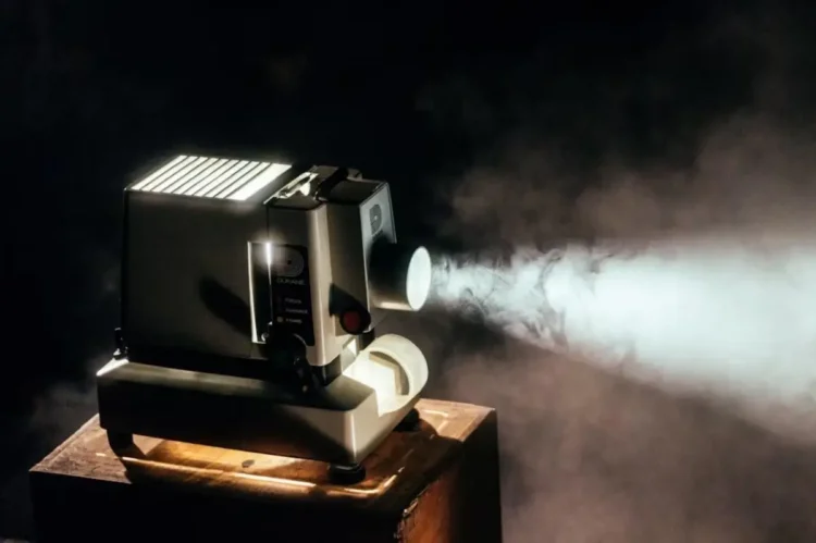 Proiettore cinematografico d'epoca acceso che proietta un fascio di luce in una stanza buia, con il fumo che rende visibile il raggio luminoso