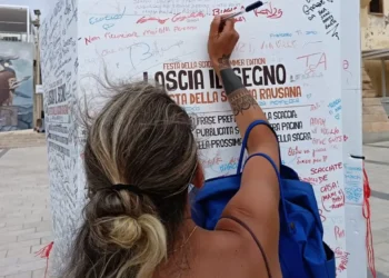 Una turista firma e lascia un messaggio su un totem ricoperto di scritte davanti all'Info Point di Marina di Ragusa.