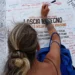 Una turista firma e lascia un messaggio su un totem ricoperto di scritte davanti all'Info Point di Marina di Ragusa.