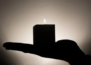Sagoma di una mano che regge una candela accesa davanti a uno sfondo scuro