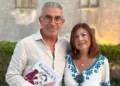 Salvatore Battaglia e Salvatrice Corallo posano insieme tenendo in mano il libro "Raccontami di te" davanti a un edificio in pietra.