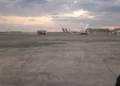 Pista dell'aeroporto di Catania al tramonto con aerei fermi ai gate e mezzi di servizio sul piazzale.