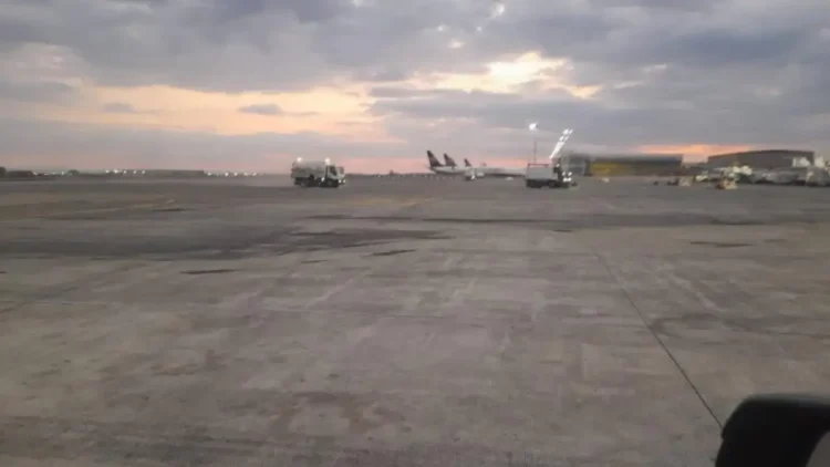 Pista dell'aeroporto di Catania al tramonto con aerei fermi ai gate e mezzi di servizio sul piazzale.