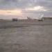 Pista dell'aeroporto di Catania al tramonto con aerei fermi ai gate e mezzi di servizio sul piazzale.