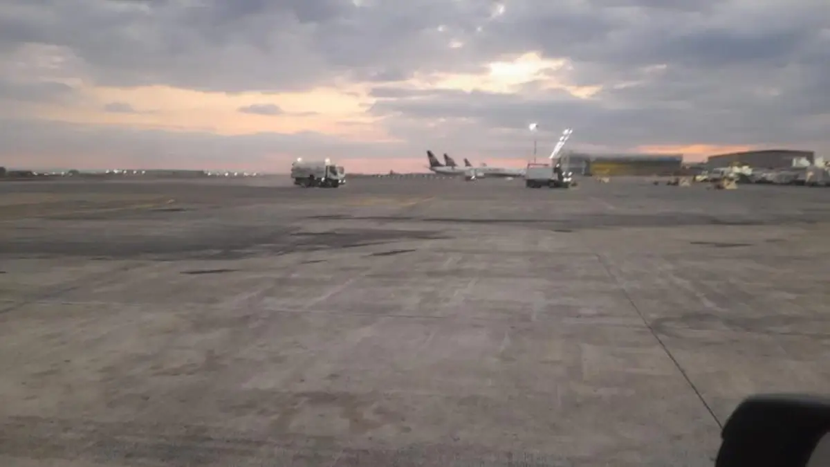 Pista dell'aeroporto di Catania al tramonto con aerei fermi ai gate e mezzi di servizio sul piazzale.