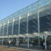 Facciata in vetro e acciaio del terminal dell'aeroporto di Catania Fontanarossa con passeggeri e carrelli portabagagli all'esterno.