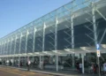 Facciata in vetro e acciaio dell'aeroporto di Catania Fontanarossa con passeggeri e carrelli portabagagli all'esterno