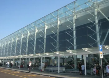 Facciata in vetro e acciaio dell'aeroporto di Catania Fontanarossa con passeggeri e carrelli portabagagli all'esterno