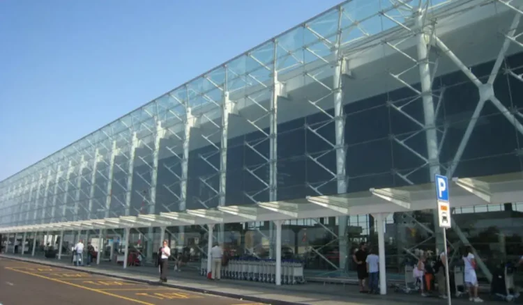Facciata in vetro e acciaio dell'aeroporto di Catania Fontanarossa con passeggeri e carrelli portabagagli all'esterno