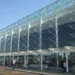 Facciata in vetro e acciaio dell'aeroporto di Catania Fontanarossa con passeggeri e carrelli portabagagli all'esterno