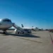 Pista dell'aeroporto di Comiso con due aerei di linea in sosta davanti al terminal, cielo sereno.