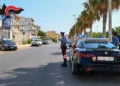 Due auto dei Carabinieri e due militari in uniforme durante un controllo su una strada alberata di Ragusa.