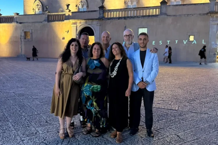 Sette membri del direttivo AIDC Ragusa in posa davanti a un edificio storico illuminato durante un evento serale