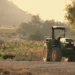 Trattore verde fermo ai margini di un campo coltivato, tra alberi e vegetazione rurale