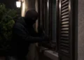 Uomo incappucciato forza con un attrezzo la persiana di una finestra al buio, di notte