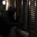 Uomo incappucciato forza con un attrezzo la persiana di una finestra al buio, di notte