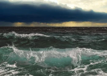 Mare mosso con onde che si frangono sulla riva e cielo coperto da nubi temporalesche scure all'orizzonte.