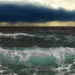Mare mosso con onde che si frangono sulla riva e cielo coperto da nubi temporalesche scure all'orizzonte.