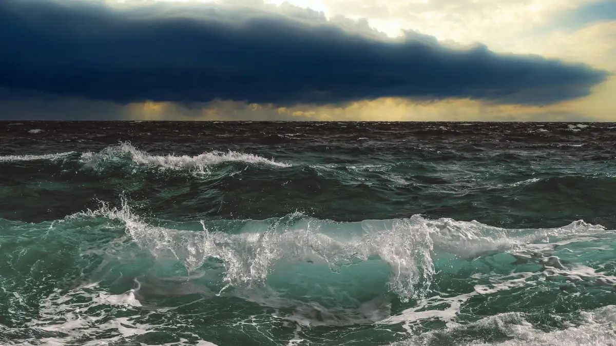 Mare mosso con onde che si frangono sulla riva e cielo coperto da nubi temporalesche scure all'orizzonte.
