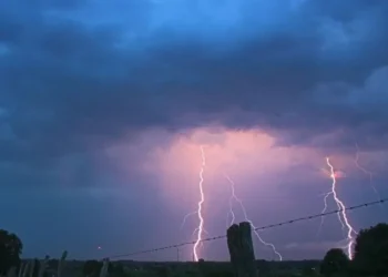 Due fulmini colpiscono la pianura al crepuscolo, cielo coperto da nuvole temporalesche illuminate di viola e arancione