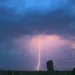 Due fulmini colpiscono la pianura al crepuscolo, cielo coperto da nuvole temporalesche illuminate di viola e arancione