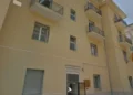 Facciata di un edificio popolare con balconi in muratura, persiane chiuse e bandiere esposte, a Pozzallo.