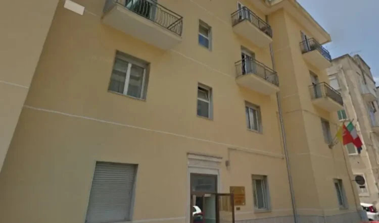 Facciata di un edificio popolare con balconi in muratura, persiane chiuse e bandiere esposte, a Pozzallo.