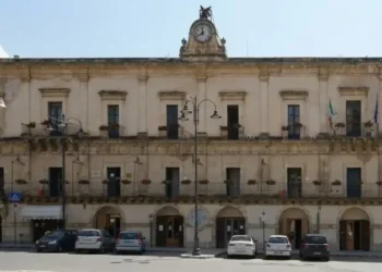 Facciata di Palazzo San Domenico a Modica, sede del Comune, con orologio e bandiere italiane ed europee