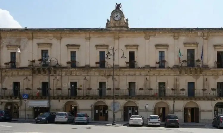 Facciata di Palazzo San Domenico a Modica, sede del Comune, con orologio e bandiere italiane ed europee