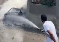 Un uomo usa una manichetta per dirigere acqua verso un veicolo avvolto dal fumo