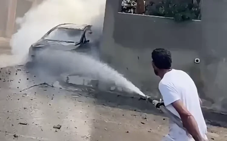 Un uomo usa una manichetta per dirigere acqua verso un veicolo avvolto dal fumo
