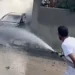 Un uomo usa una manichetta per dirigere acqua verso un veicolo avvolto dal fumo