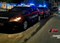 Due auto dei Carabinieri con lampeggianti blu accesi in una strada di notte, logo Carabinieri Ragusa in basso a destra.