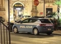 Auto della Polizia di Stato ferma di notte in una via del centro, con passanti sullo sfondo