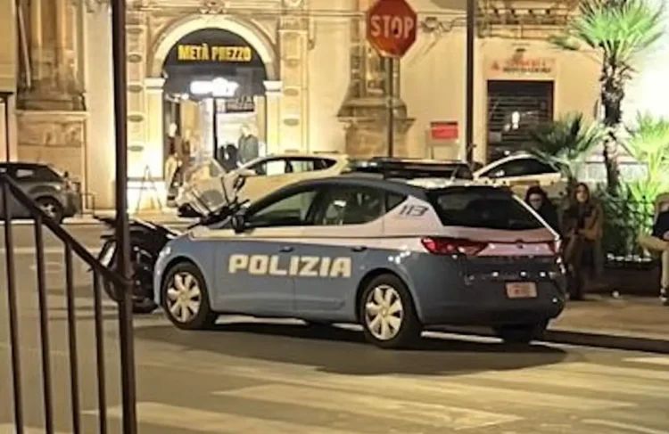 Auto della Polizia di Stato ferma di notte in una via del centro, con passanti sullo sfondo