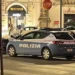 Auto della Polizia di Stato ferma di notte in una via del centro, con passanti sullo sfondo