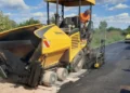 Vibrofinitrice stende asfalto fresco su una strada, sullo sfondo un rullo compattatore al lavoro