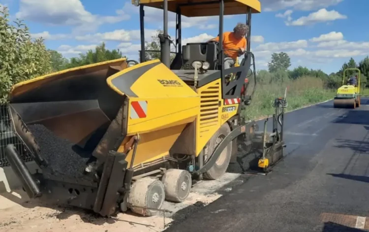 Vibrofinitrice stende asfalto fresco su una strada, sullo sfondo un rullo compattatore al lavoro