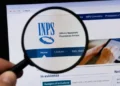 Lente d'ingrandimento inquadra il logo dell'Inps sullo schermo di un computer, mano in primo piano