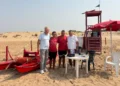 Quattro persone davanti alla torretta di salvataggio e al pattino rosso su una spiaggia di Donnalucata, a Scicli.