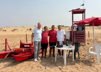 Quattro persone davanti alla torretta di salvataggio e al pattino rosso su una spiaggia di Donnalucata, a Scicli.