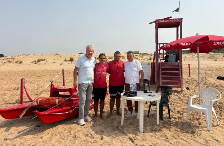 Quattro persone davanti alla torretta di salvataggio e al pattino rosso su una spiaggia di Donnalucata, a Scicli.