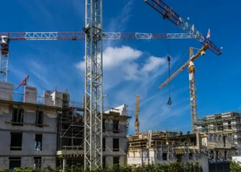 Gru e impalcature su un cantiere edile con cielo azzurro sullo sfondo, lavori di costruzione in corso