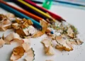Matite colorate, temperamatite e trucioli colorati su un piano bianco, materiale scolastico.