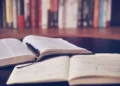 Libri aperti su un tavolo con una penna appoggiata sulle pagine e un quaderno con appunti scritti a mano in primo piano.