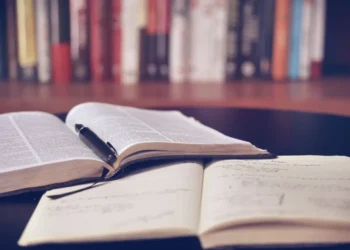 Libri aperti su un tavolo con una penna appoggiata sulle pagine e un quaderno con appunti scritti a mano in primo piano.