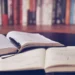 Libri aperti su un tavolo con una penna appoggiata sulle pagine e un quaderno con appunti scritti a mano in primo piano.