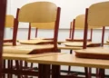 Aula scolastica vuota con file di banchi in legno su pavimento in parquet e lavagna verde sullo sfondo
