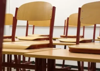 Aula scolastica vuota con file di banchi in legno su pavimento in parquet e lavagna verde sullo sfondo